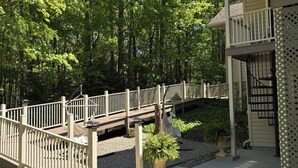 A wooden deck with a railing, a potted plant, and a building with a balcony.