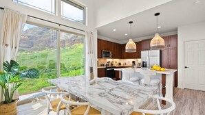 Una cocina moderna con una isla de mármol, sillas blancas y vistas al verdor.