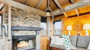 Ein gemütliches Blockhaus-Interieur mit Kamin aus Naturstein, Holzwänden und einer komfortablen Sitzecke mit Kissen.