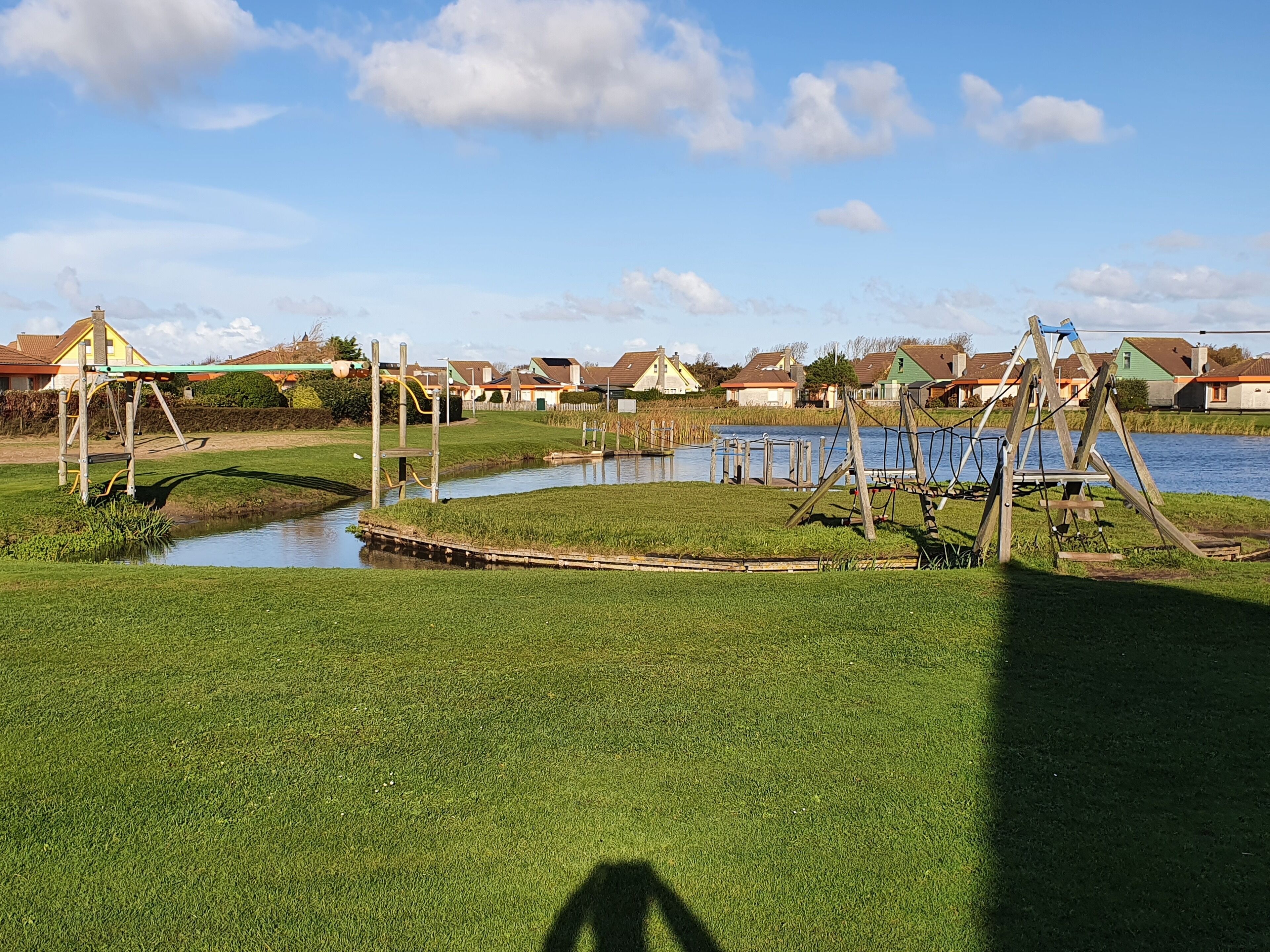 Ein Spielplatz mit Schaukeln und einem kleinen Teich, umgeben von Häusern.
