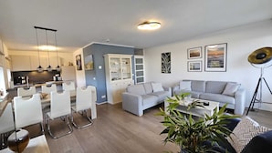 Una sala de estar moderna con un sofá gris, una mesa de centro y un comedor con sillas blancas y un armario.