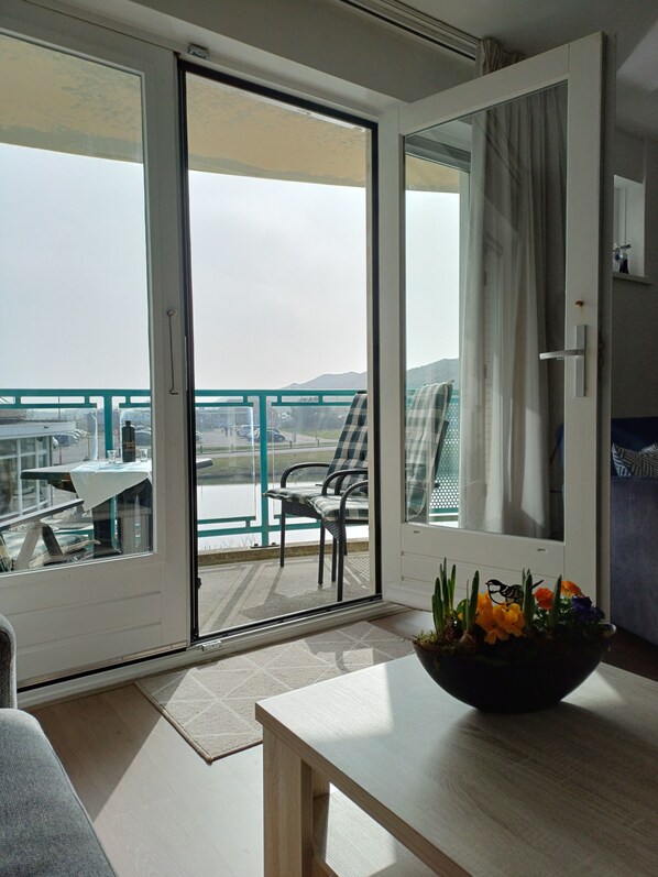 A balcony with a table and chairs, a view of the sea, and a dining area with a table and chairs.