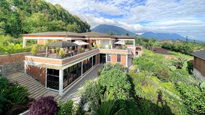 Une maison moderne dotée d’un vaste patio, entourée de jardins luxuriants et offrant une vue sur un paysage montagneux.