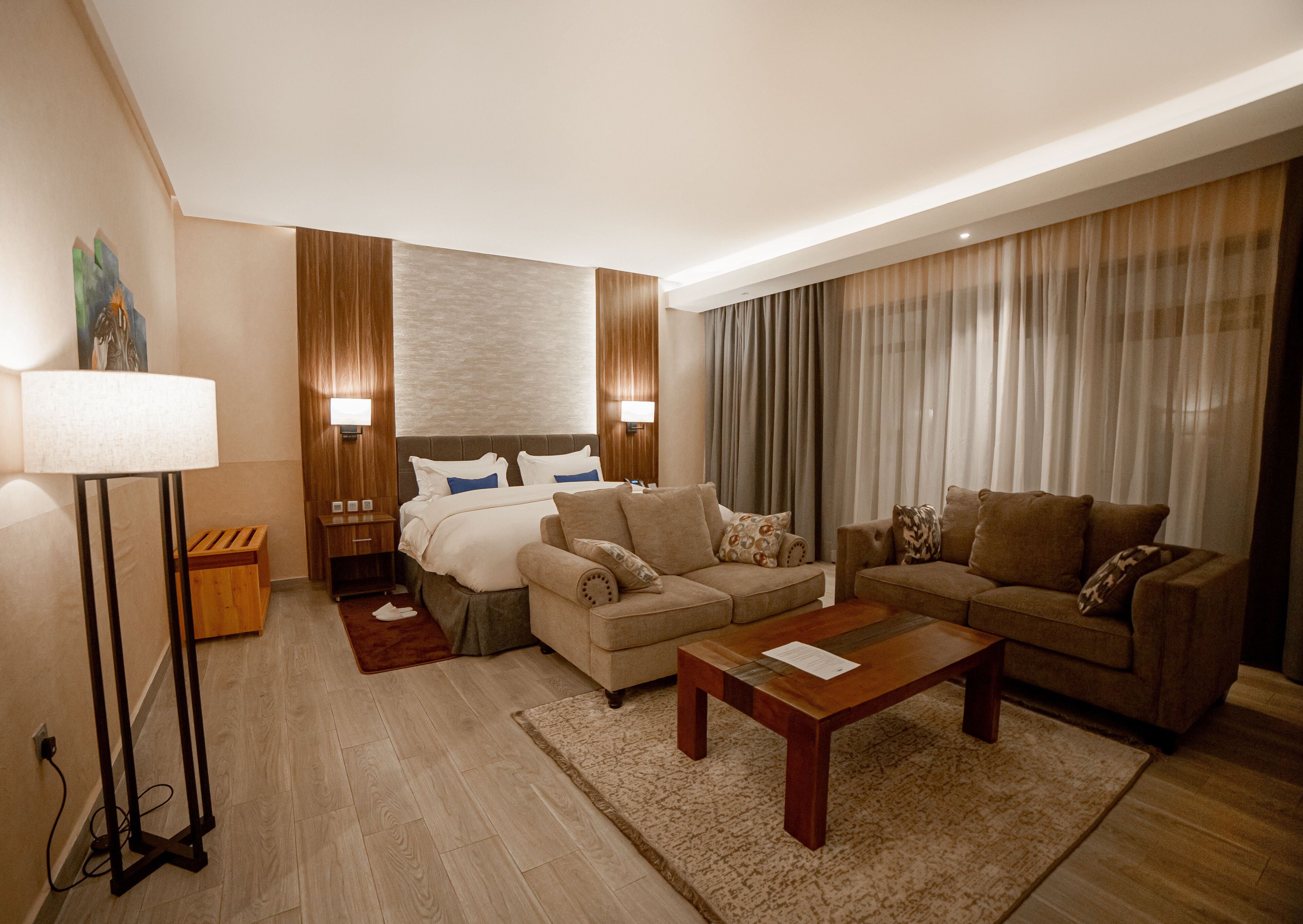 A hotel room with a bed, two sofas, a coffee table, a lamp, and a painting on the wall.