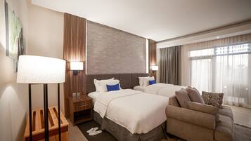 A hotel room with two beds, a sofa, a wooden nightstand, and a lamp.