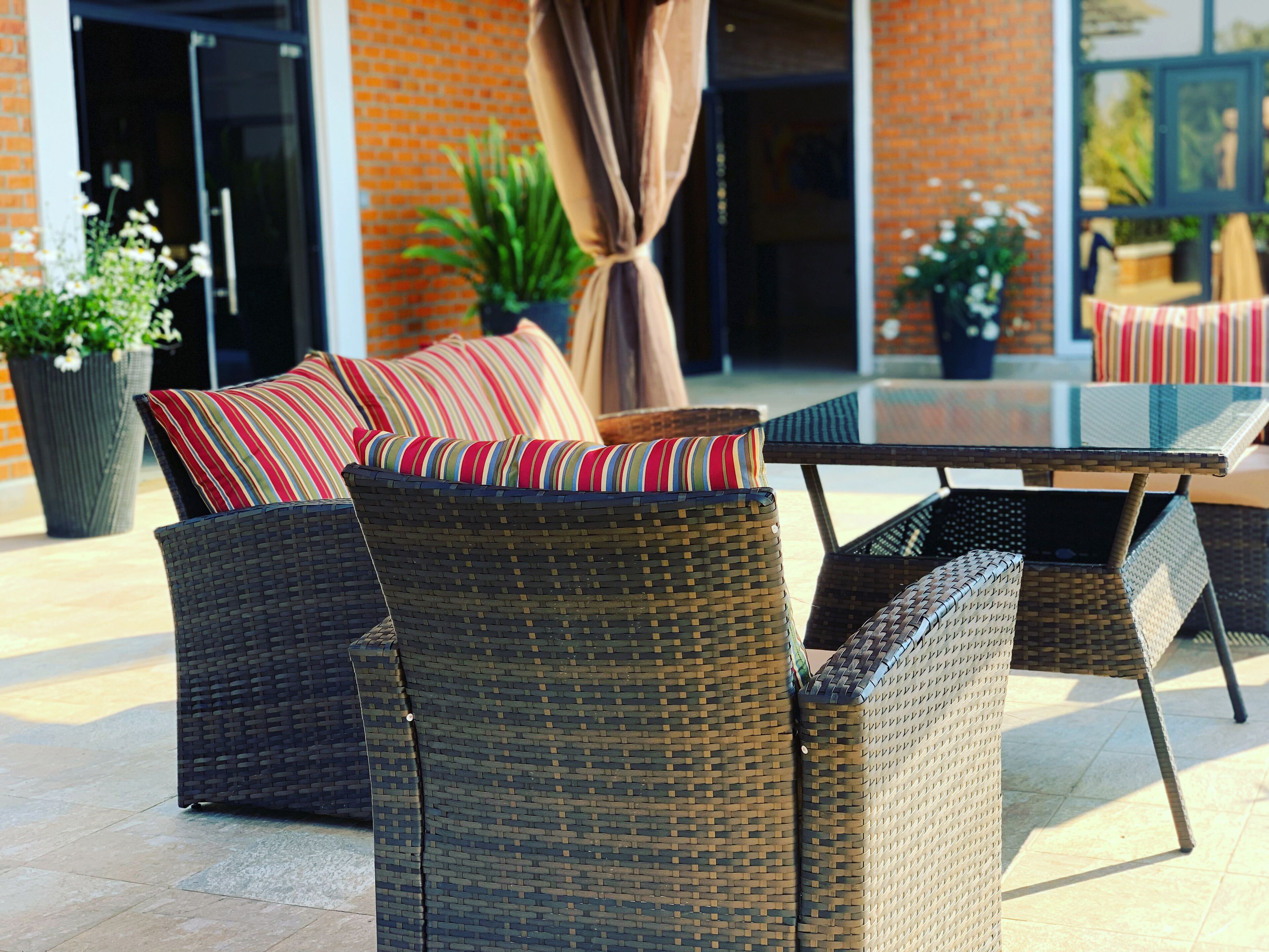 Wicker meubels met gestreepte kussens, een glazen tafel en potplanten in een patio.