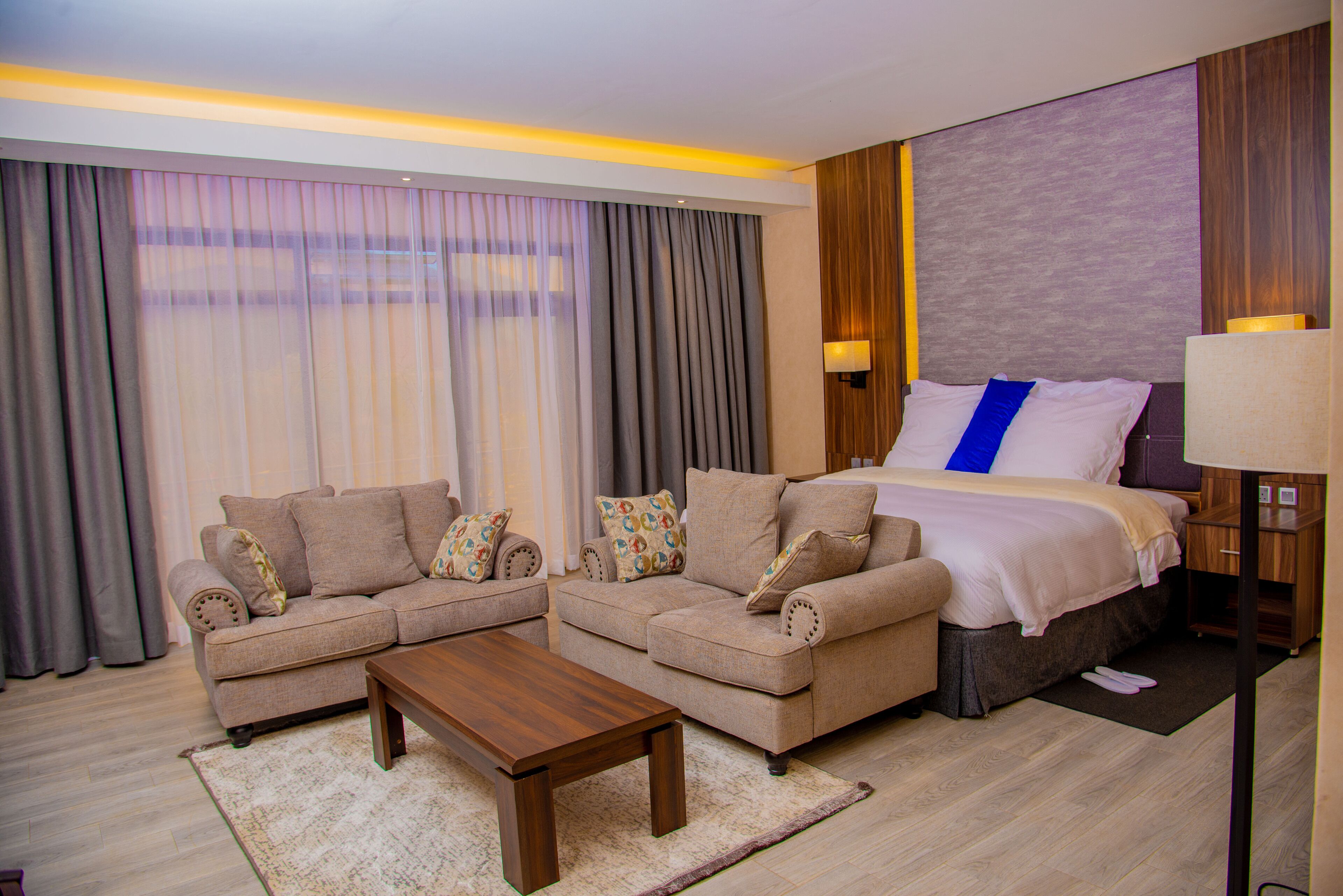 A hotel room with a bed, two sofas, a coffee table, and a nightstand with a lamp.