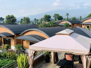 A rooftop terrace with multiple rooms, each with a curved roof and brick walls. There are outdoor seating areas with tables and chairs, surrounded by potted plants and greenery.