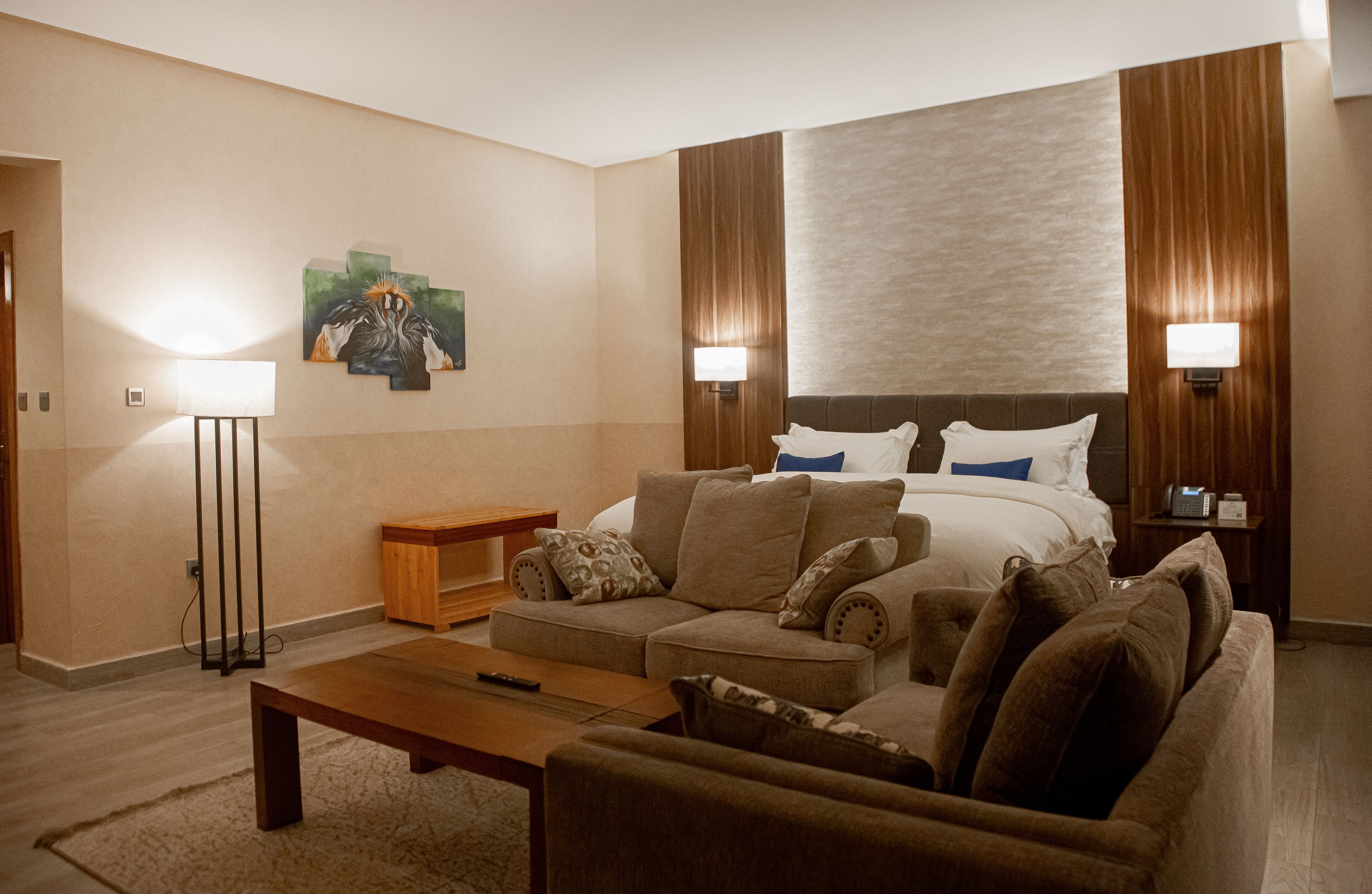 Una habitación de hotel con cama, sofá, mesa de centro, lámpara y cuadros en la pared.