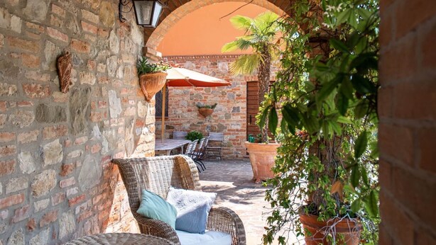 An outdoor patio with wicker furniture, a brick wall, and potted plants.