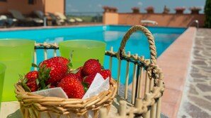 A wicker basket with strawberries and a green glass, placed by a poolside.