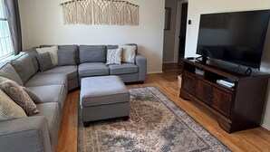Una sala de estar moderna con un sofá modular, un reposapiés y un televisor de pantalla plana sobre un mueble de madera.