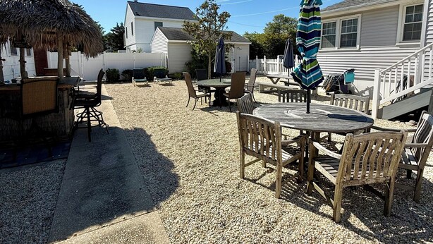 Un patio con mobiliario exterior, una estructura de paja y una casa al fondo.