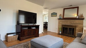Una sala de estar con televisión de pantalla plana, chimenea y un otomán grande.