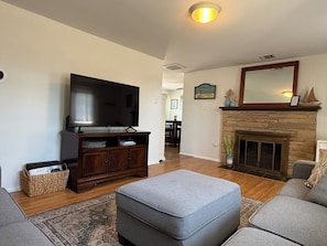 A living room with a flat-screen TV, a fireplace, and a large ottoman.