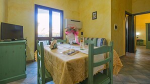 Un coin repas avec une table dressée pour deux personnes, un téléviseur posé sur un meuble et une fenêtre avec des rideaux.