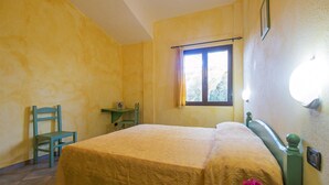 Une chambre à coucher avec un lit, une chaise, une petite table et une fenêtre avec des rideaux.