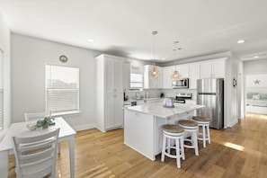 A modern kitchen with white cabinetry, a central island, bar stools, and pendant lighting.