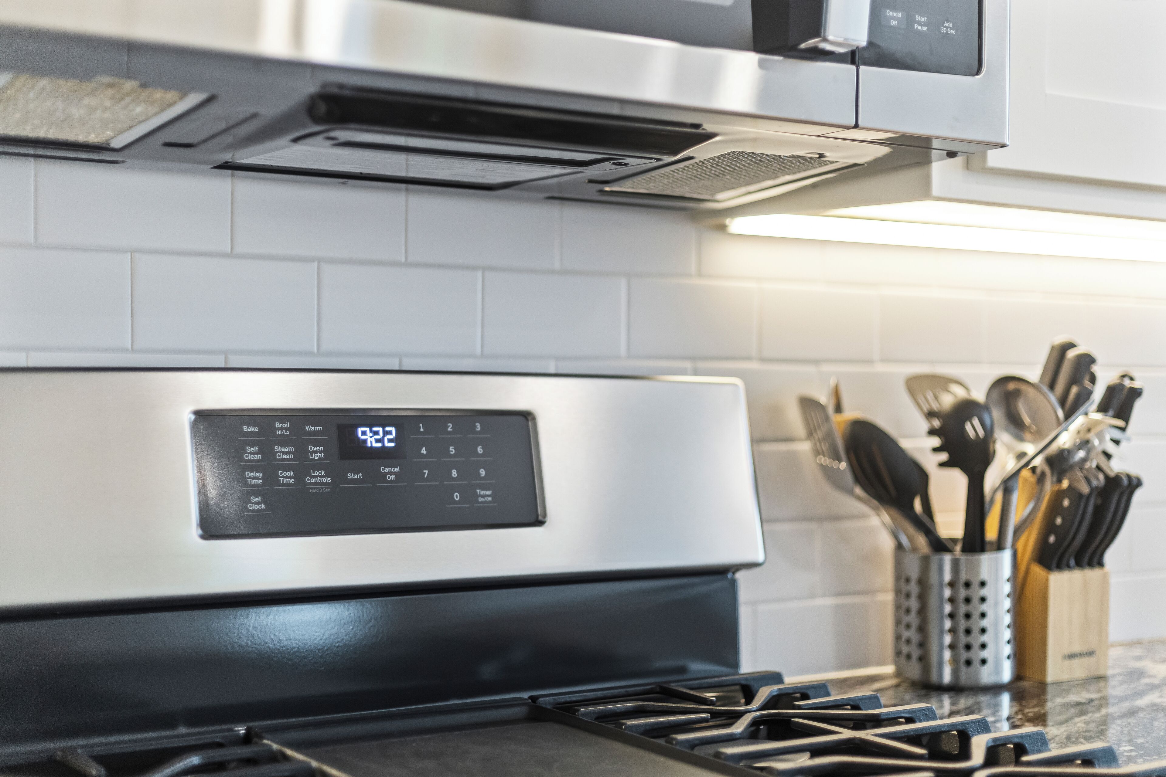 Eine moderne Küche mit Backofen aus Edelstahl, einer digitalen Bedienblende und einem Utensilienhalter auf der Arbeitsfläche.