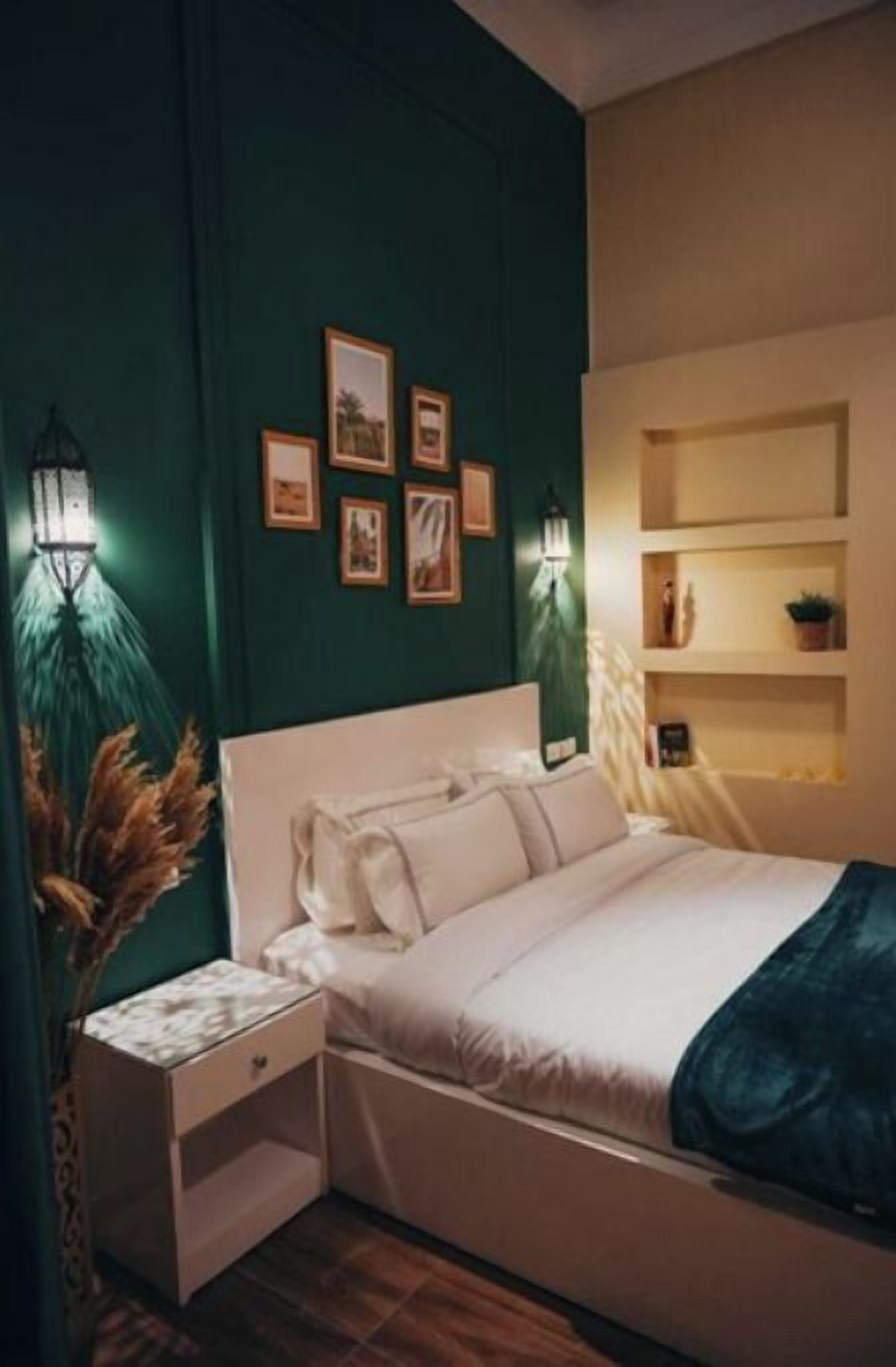 Quarto com cama branca, mesa de cabeceira, luminárias fixadas na parede e quadros emoldurados.