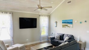 A living room with a sofa, armchair, TV, ceiling fan, and decorative items on the wall. - Coastal home walking distance to the beach (Long Beach)