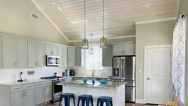 A modern kitchen with a central island, bar stools, stainless steel appliances, and a wooden ceiling. - Coastal home walking distance to the beach (Long Beach)