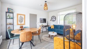 A modern living room with a wooden dining table, blue and yellow sofas, and a TV.