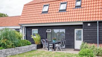 Un bâtiment doté d’un toit recouvert de tuiles rouges, d’une façade noire et d’un patio aménagé avec une table et des chaises.