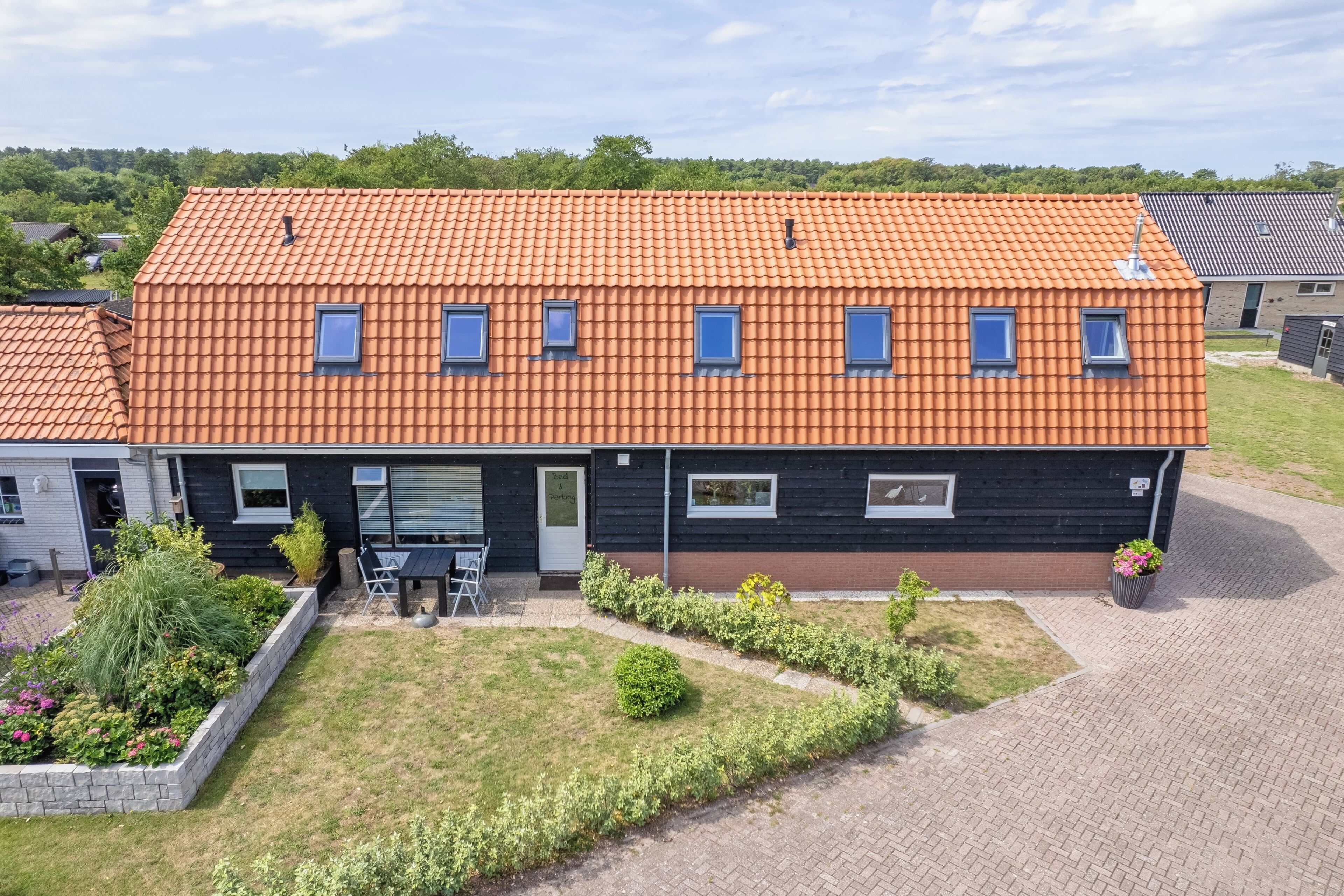 Une maison à deux étages, avec un toit en tuiles, un porche à l’avant et un jardin aménagé.