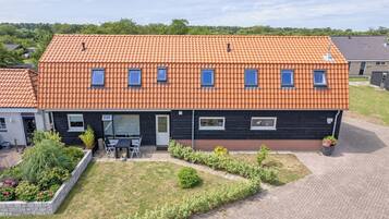 Une maison à deux étages, avec un toit en tuiles, un porche à l’avant et un jardin aménagé.