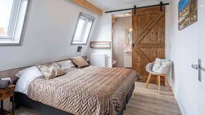 A bedroom with a bed, a chair, a wooden door, and a window.