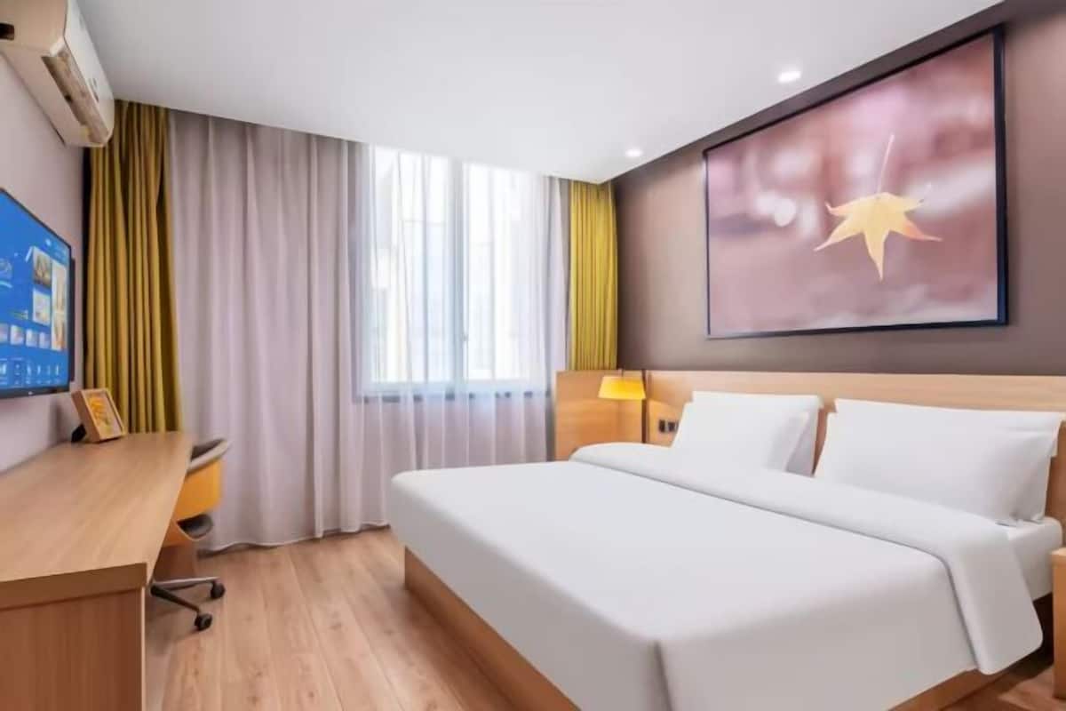 A hotel room with a bed, a desk, a chair, a TV, and a window with curtains.