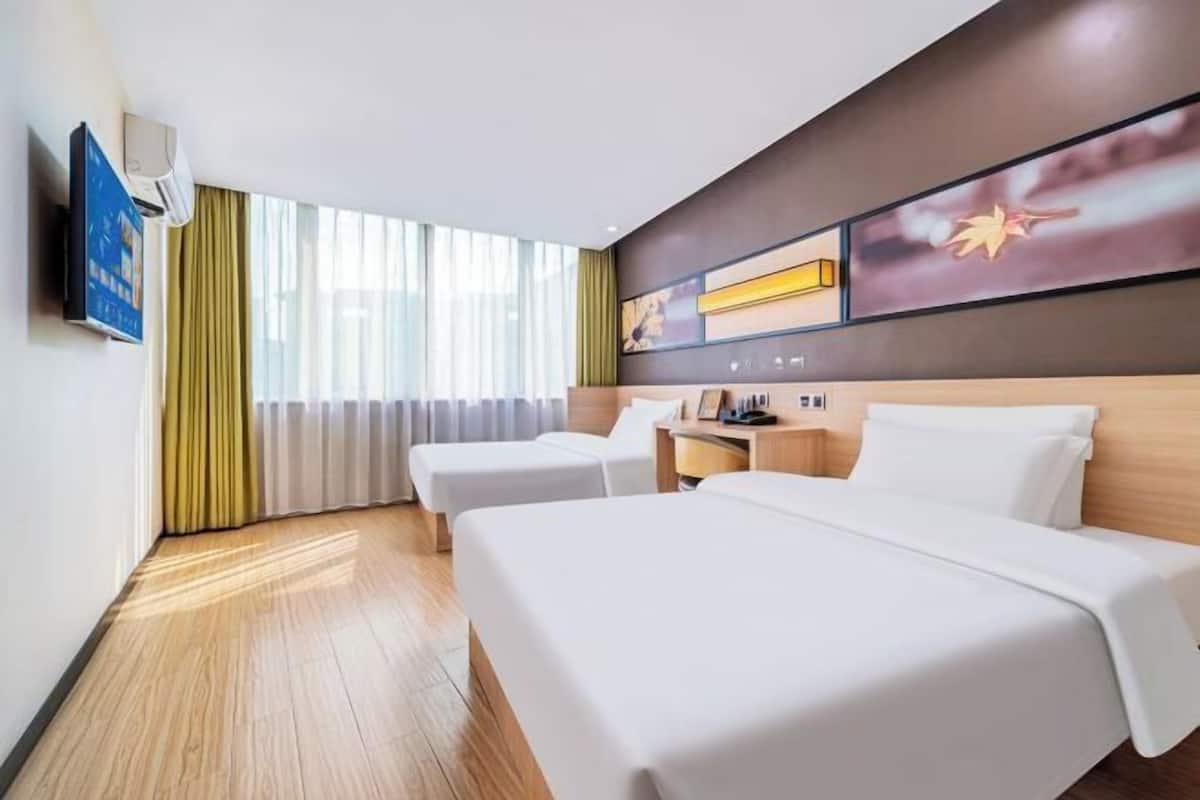 A hotel room with two beds, a desk, a chair, a TV, and a large window with curtains.