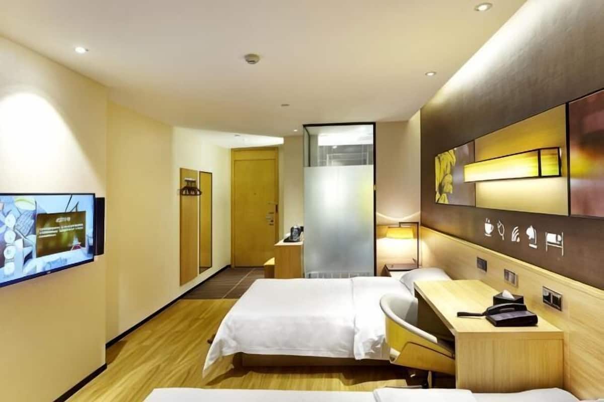 A hotel room with two beds, a desk, a TV, and a mirror.