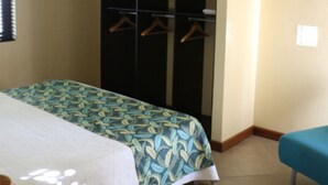 Un dormitorio con cama, armario, banca y perchero.