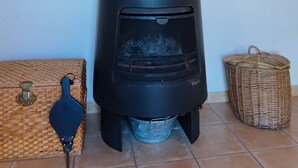 A black wood stove with a chimney, a woven basket, and a wicker chest of drawers.