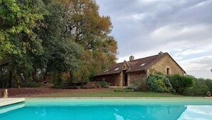 A stone house with a swimming pool, surrounded by trees and greenery.
