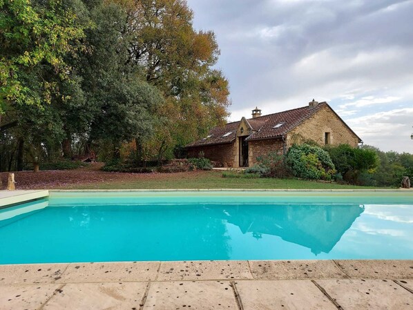 A stone house with a swimming pool, surrounded by trees and greenery.