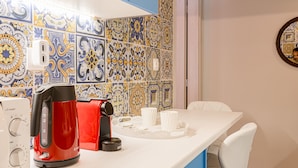 Uma cozinha com azulejos coloridos, uma chaleira vermelha, xícaras brancas e uma tomada.