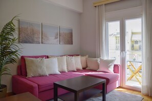 A pink sofa with white cushions, a dark wooden coffee table, and a potted plant.