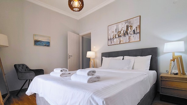 Quarto de hotel com uma cama grande, uma cadeira, mesa de cabeceira, abajur e um quadro na parede.