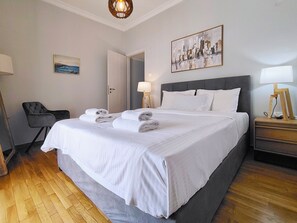 Une chambre d’hôtel avec un grand lit, une chaise, une table de chevet, une lampe et un tableau au mur.