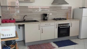 A modern kitchen with a gas stove, oven, and a coffee maker. There is a small refrigerator and a cart with storage bins. - APPT T2 Cirique (Anses d'Arlet)