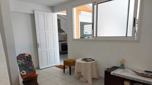 A compact living space with a kitchenette, a dining area, and a seating area with a patterned chair and ottoman. - APPT T2 Cirique (Anses d'Arlet)