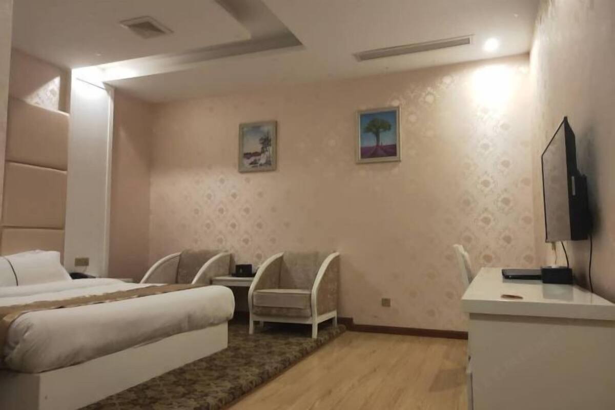 A bedroom with a bed, two chairs, a desk, and a TV.