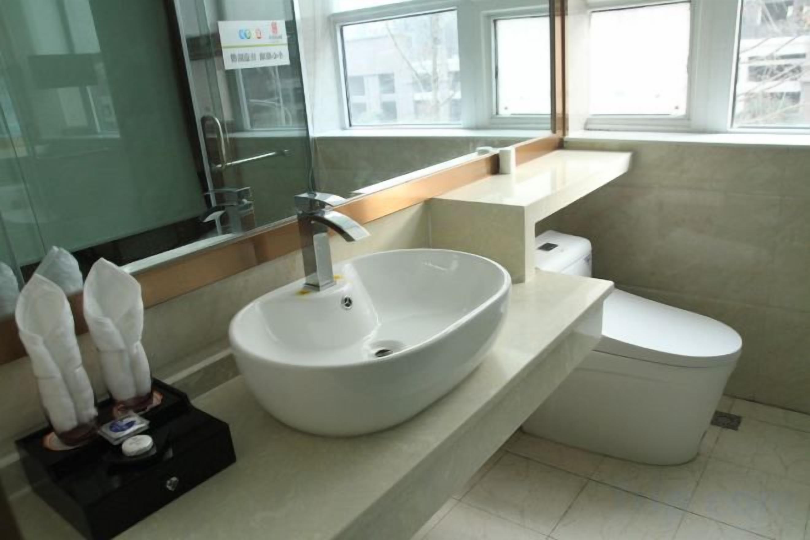 A modern bathroom with a white sink, a toilet, and a window providing natural light.