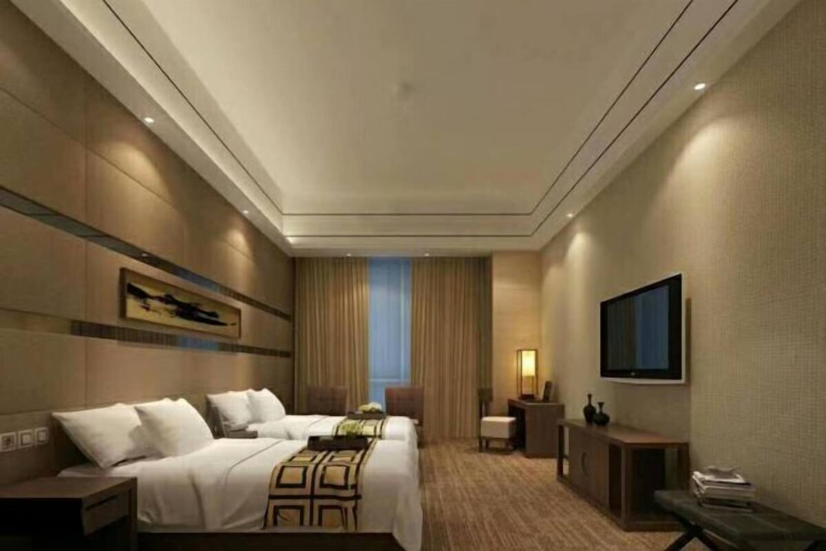 A hotel room with two beds, a television, a desk, and a window with curtains.