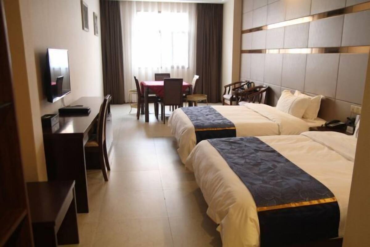 A hotel room with two beds, a desk, a TV, and a dining table with chairs.