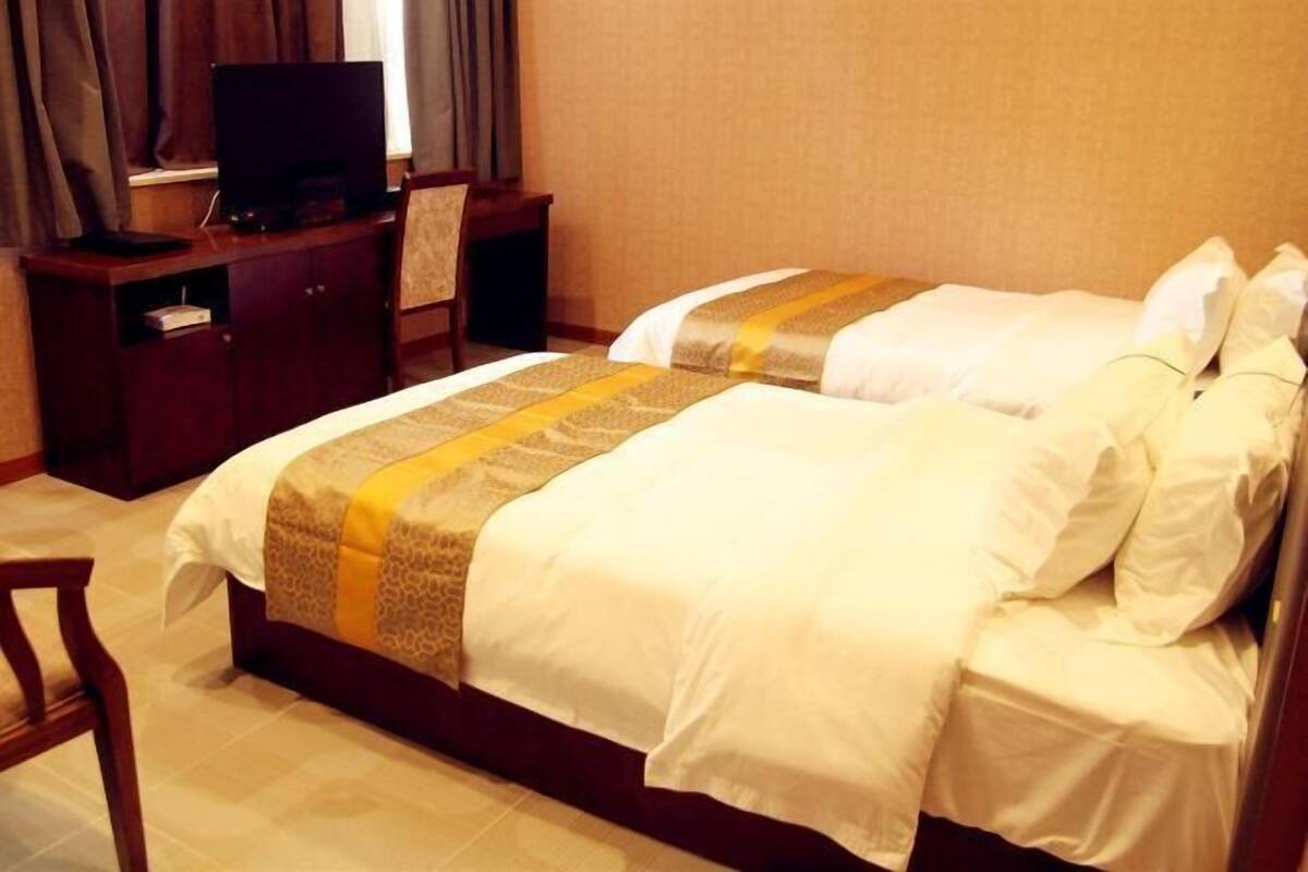 A hotel room with two beds, a TV on a wooden cabinet, and a chair.