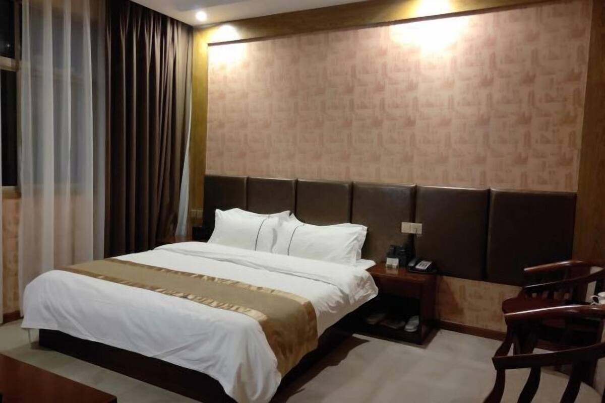 A hotel room with a large bed, a wooden headboard, a bedside table with a phone, and a chair.